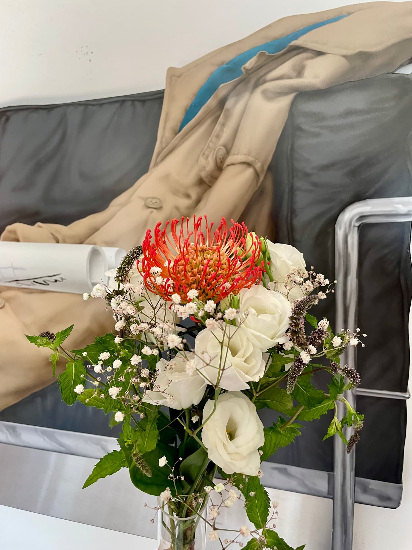 Bouquet of protea, white roses and mint in front of a large painting of a figure in a trench coat