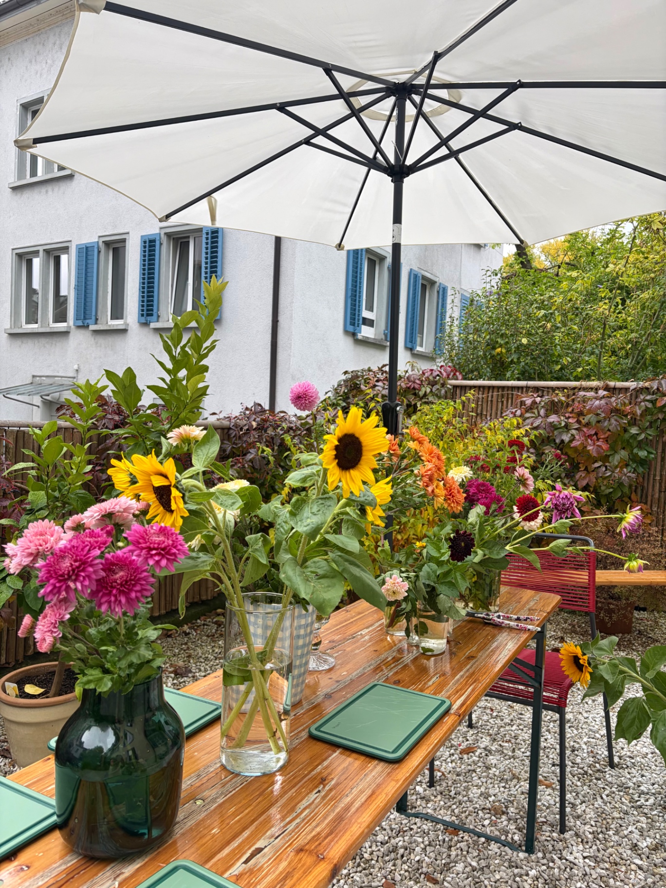 Long wooden table outdoors lined with vases of freshly picked garden flowers — sunflowers, dahlias and chrysanthemums