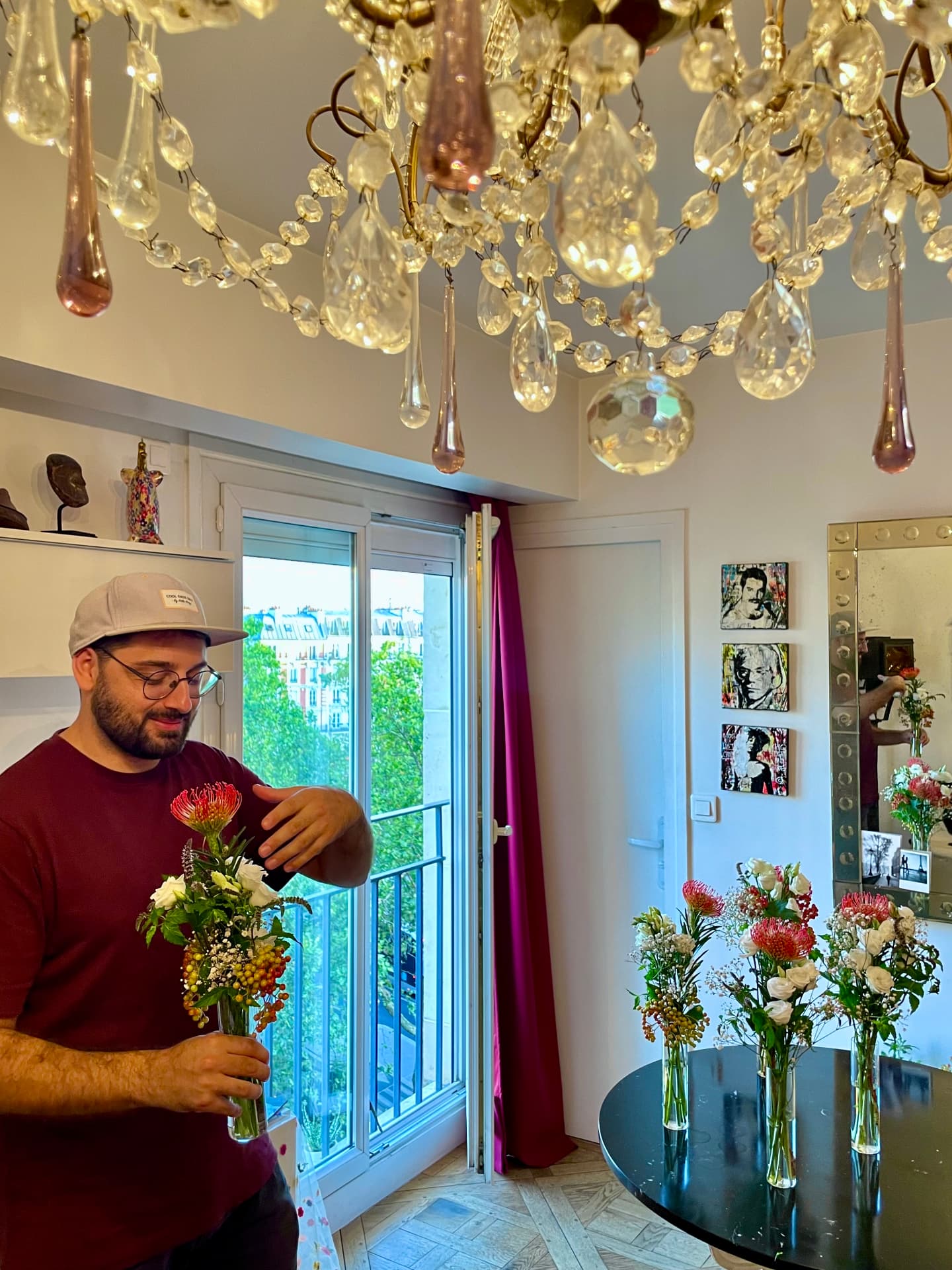 Guest arranging a bouquet of pincushion protea and white lisianthus beneath a crystal chandelier in a Paris apartment