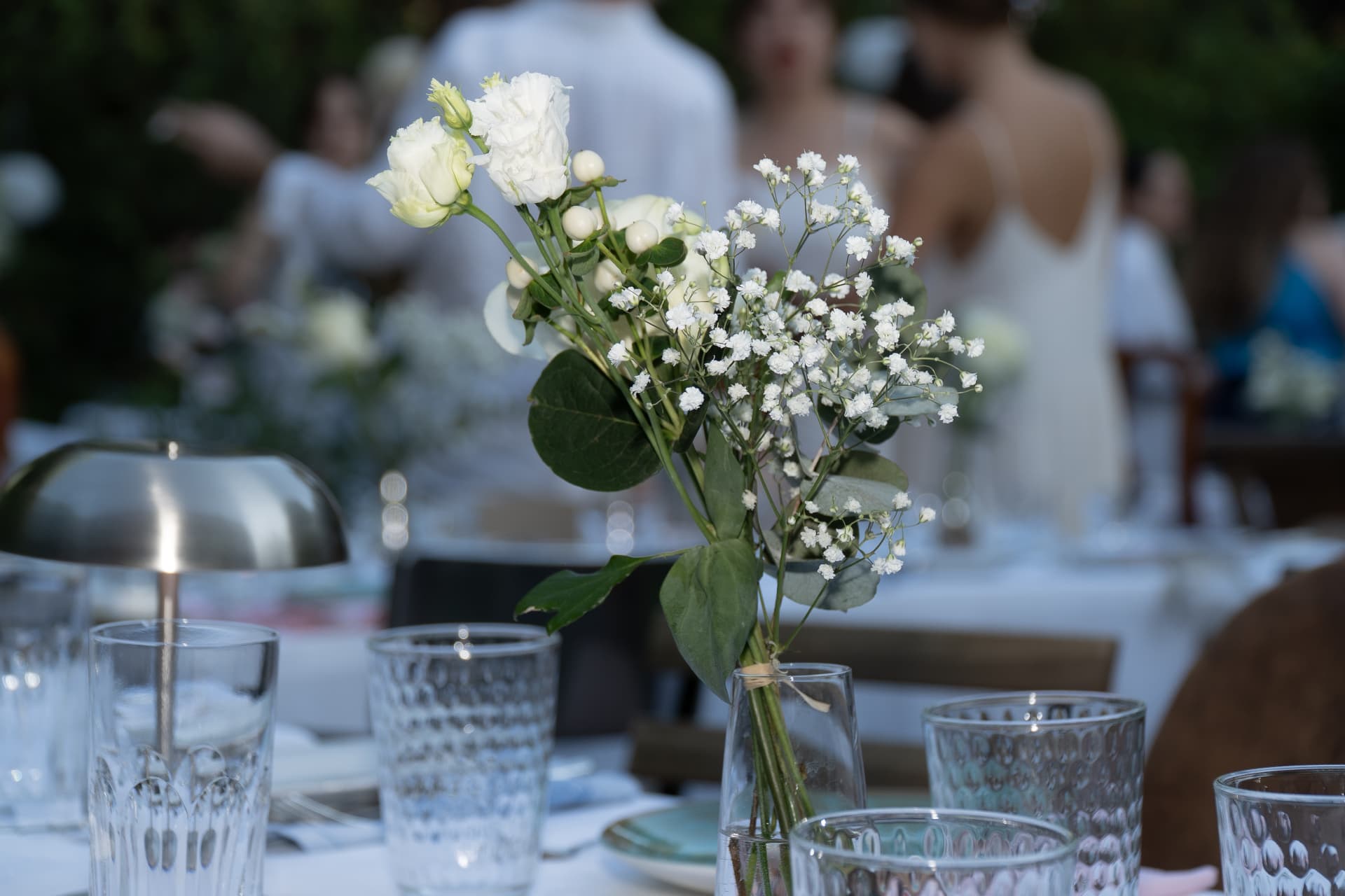 Bud vase with white lisianthus, roses, hypericum berries and gypsophila on the dinner table