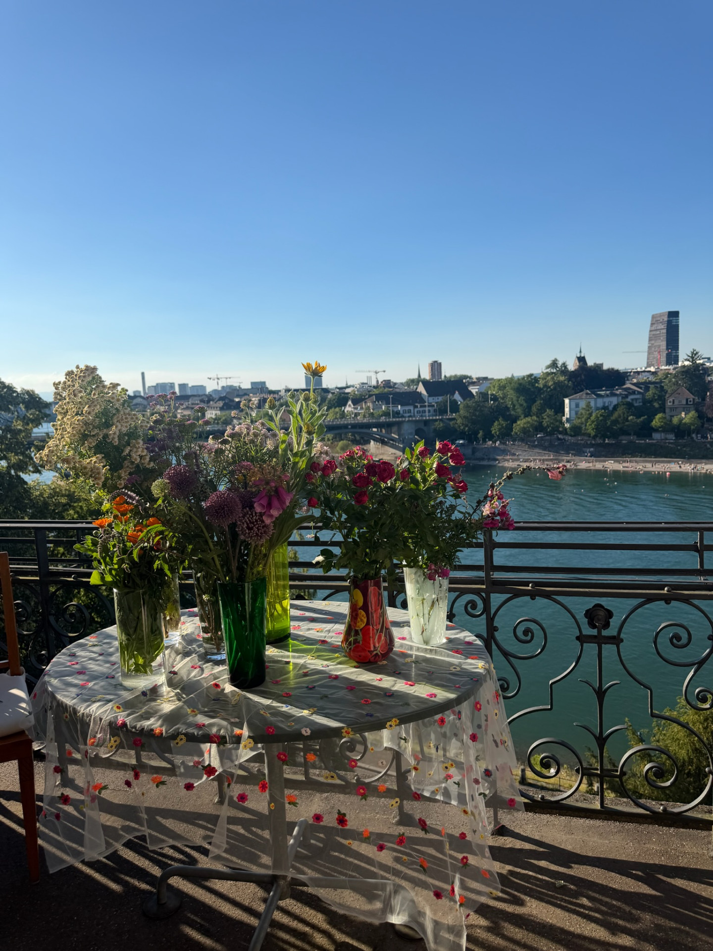 Row of wildflower arrangements in glass vases on a floral tablecloth overlooking the Rhine and Basel skyline