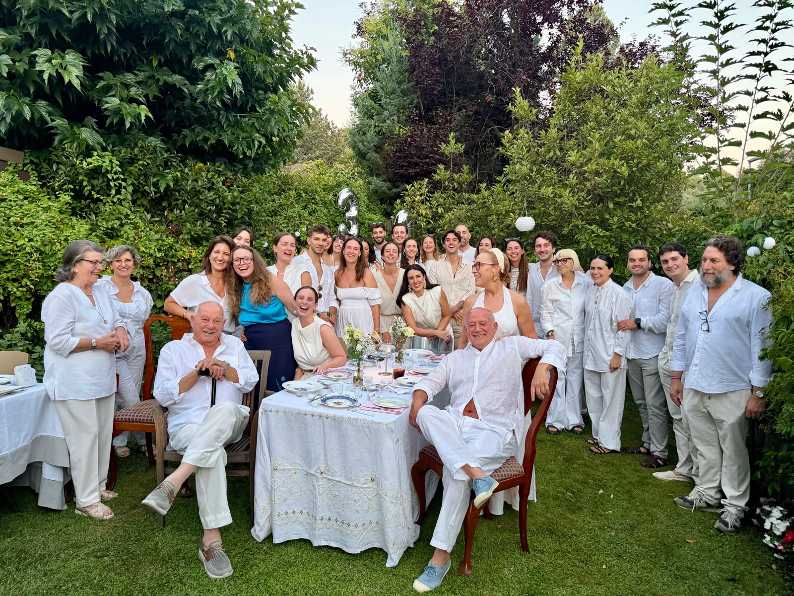 Guests gathered in the garden for the Madrid birthday celebration, dressed in white around a long dinner table