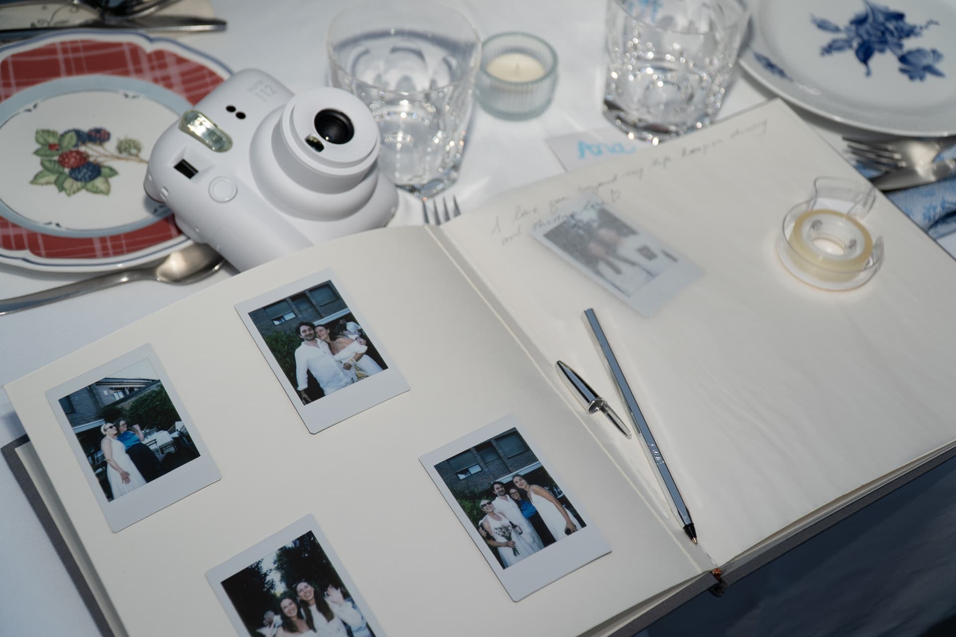 Open guest book with instant polaroid photographs, a pen and an instant camera on the dinner table