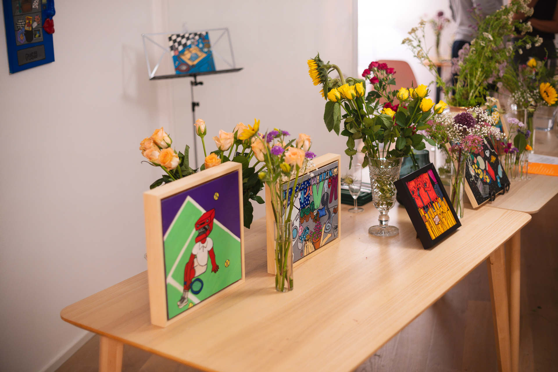 Framed artworks and flower arrangements of peach roses, yellow spray roses and sunflowers lining a wooden table at the Zurich Seefeld Session
