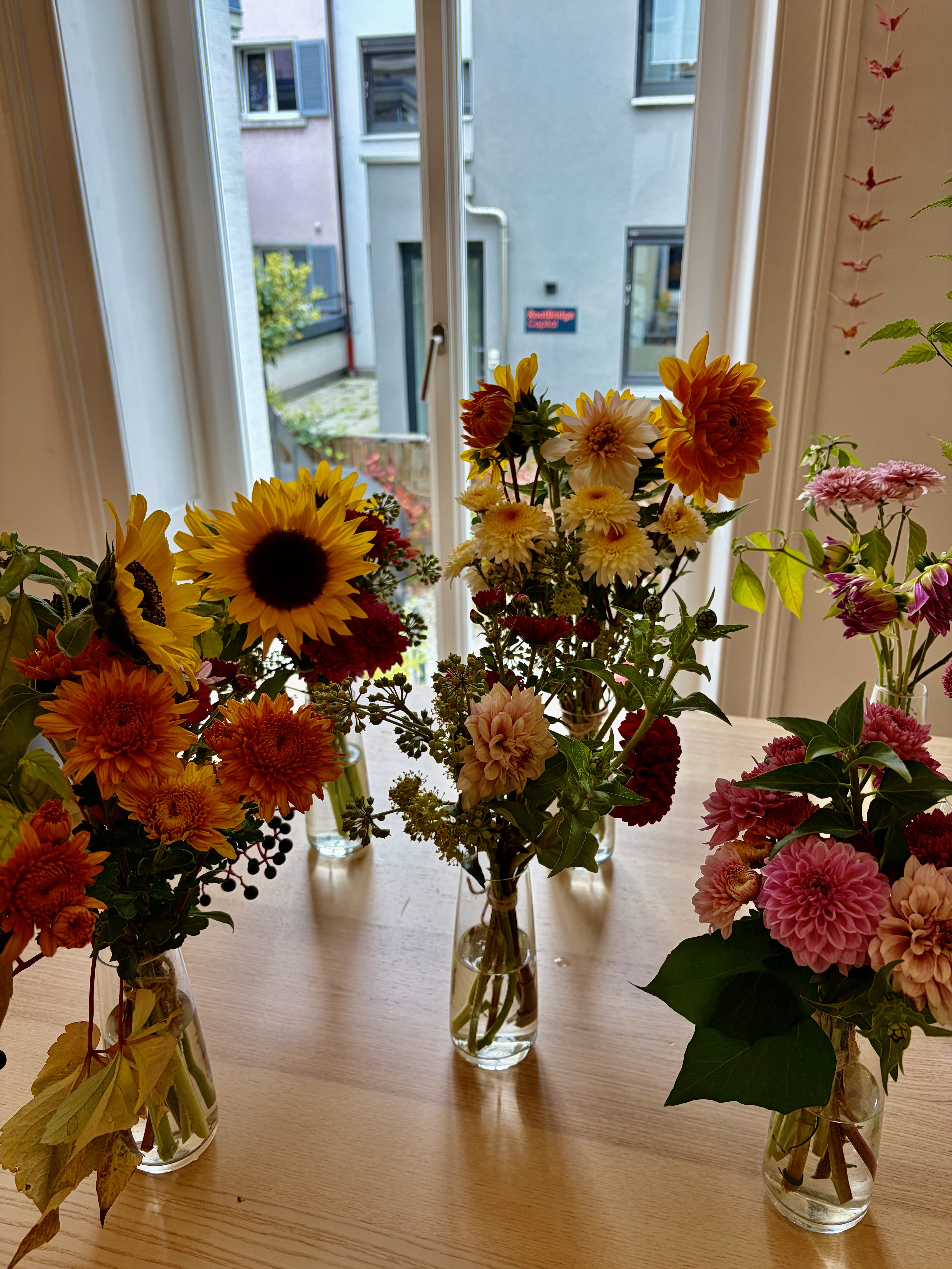 Row of autumn arrangements — dahlias, sunflowers, chrysanthemums and berries — lining a wooden table at the private birthday event