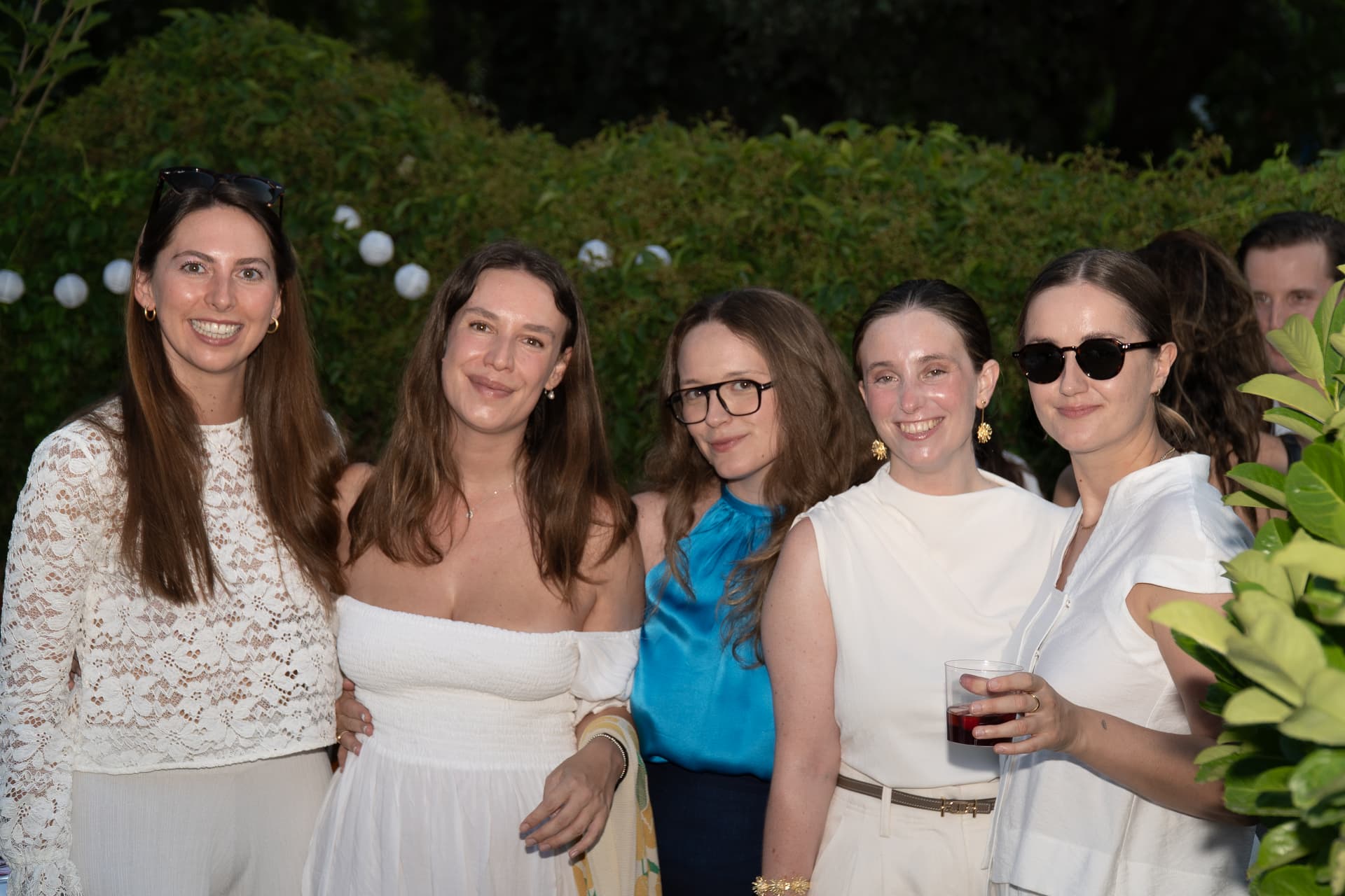 Five guests dressed in white smiling together in the garden at the Madrid birthday celebration