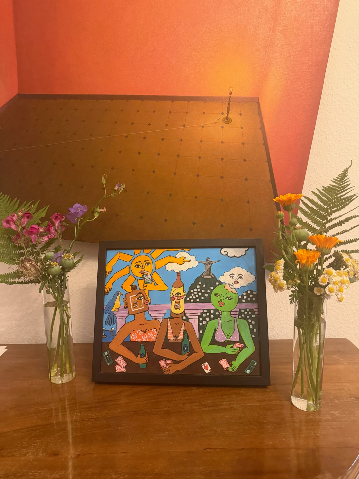 Framed Rio-inspired painting with sun and Christ the Redeemer flanked by two bud vases of snapdragon, campanula, calendula and chamomile on a wooden console