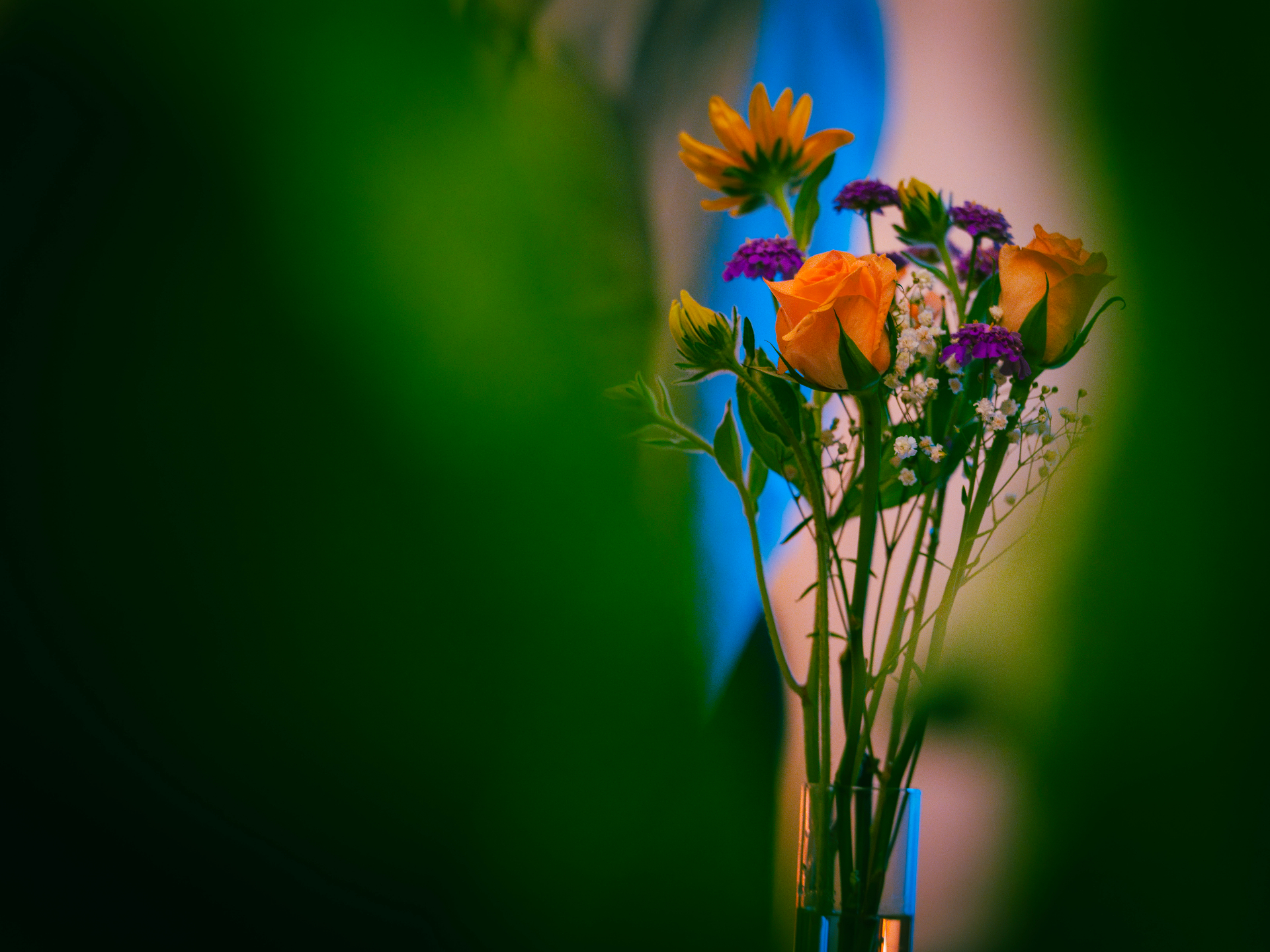 Bud vase with orange spray roses, rudbeckia and purple verbena against a soft green backdrop