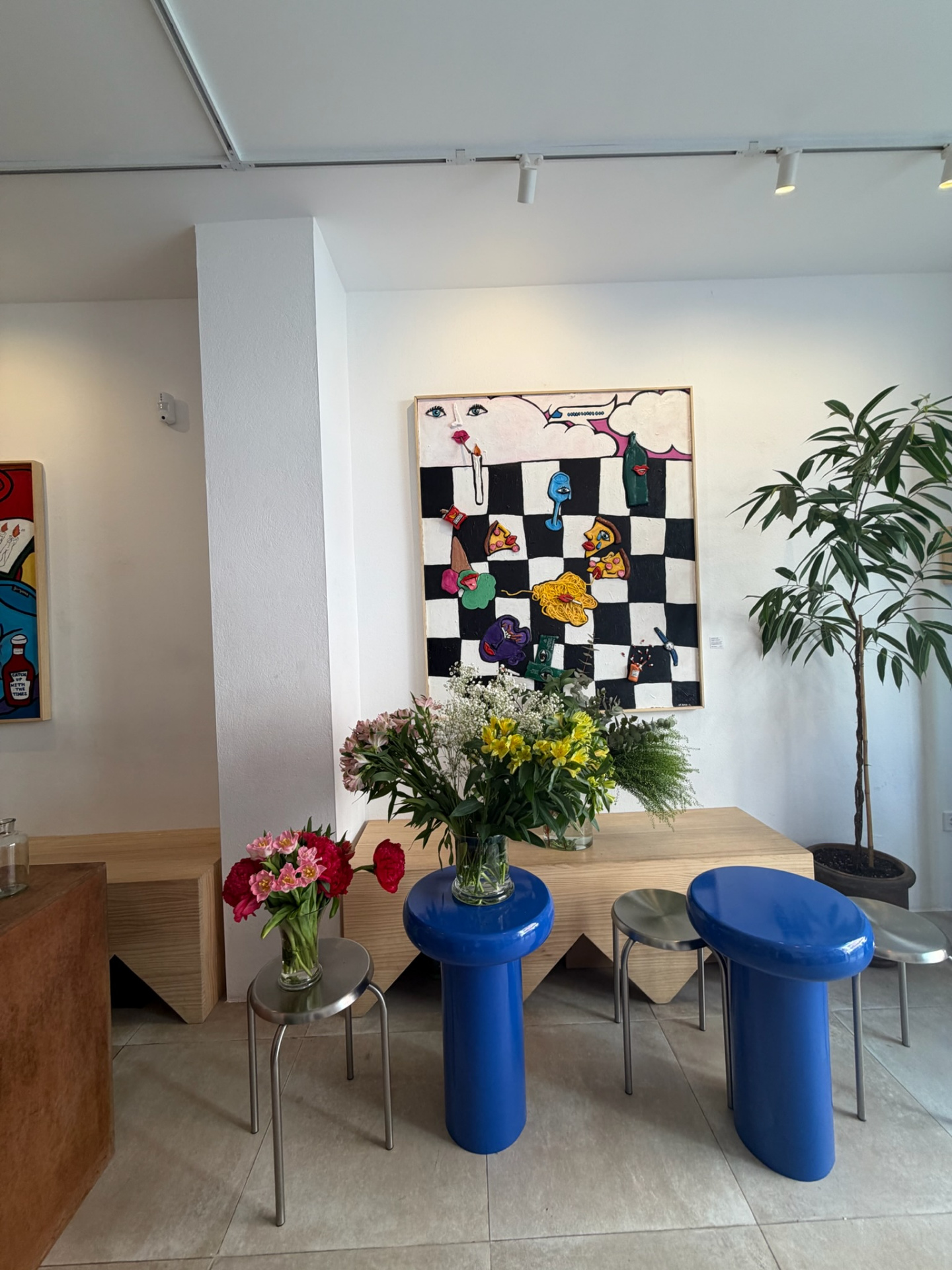 Gallery arrangement of alstroemeria, carnations, tulips and gypsophila on blue plinth beside pop-art canvas